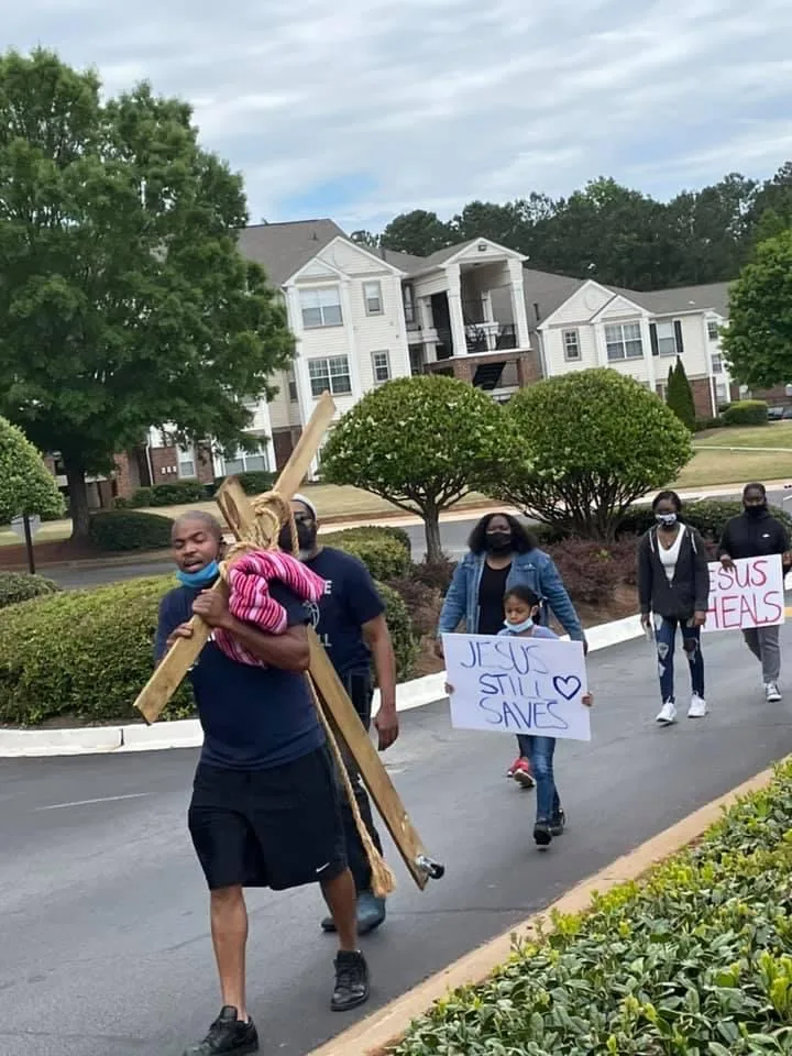 A street march with a cross and signs that read Jesus still saves